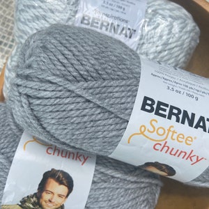 May include: Three skeins of Bernat Softee Chunky yarn in a wooden bowl. Two skeins are gray, and one is a light gray and white mix. Each skein is labeled with the brand name, yarn type, and weight of 3.5 oz (100 g).