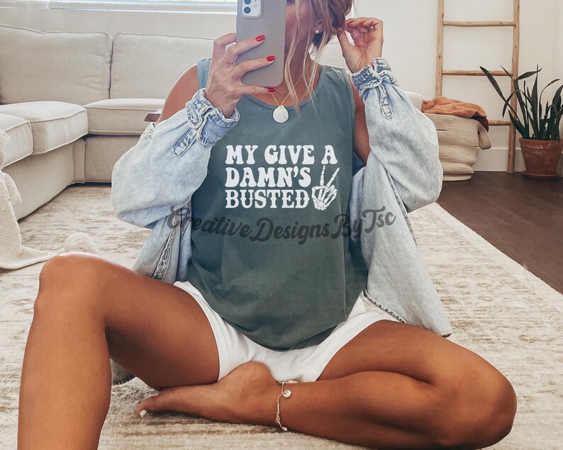 May include: A green tank top with the text "My Give A Damn's Busted" in white lettering and a peace sign with a skeleton hand. The tank top is being worn by a person.