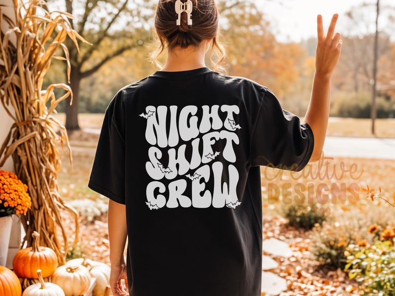 May include: A black short-sleeved t-shirt featuring white text on the back that reads "NIGHT SHIFT CREW" in a wavy, retro-inspired font. Small white bat silhouettes are scattered around the lettering, which is centered on the back of the shirt.