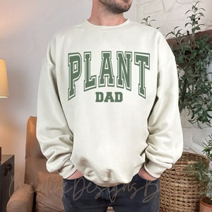 May include: A cream colored sweatshirt with the text "PLANT DAD" in green letters.