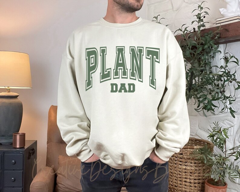 May include: A cream colored sweatshirt with the text "PLANT DAD" in green letters.