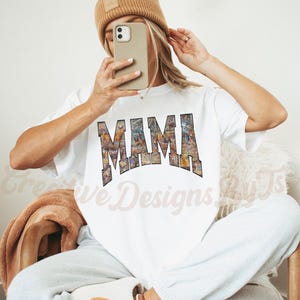 Puede incluir: Camiseta blanca con un estampado gr&aacute;fico de la palabra "MAMA" en un dise&ntilde;o abstracto colorido.