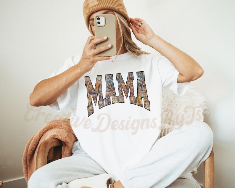 Puede incluir: Camiseta blanca con un estampado gr&aacute;fico de la palabra "MAMA" en un dise&ntilde;o abstracto colorido.