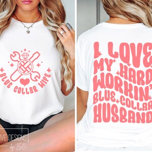 May include: A white t-shirt with a pink design on the front that says "Blue Collar Wife" with a wrench and screwdriver crossed over a ring with a diamond. The back of the shirt has a pink design that says "I Love My Hard Workin' Blue Collar Husband".