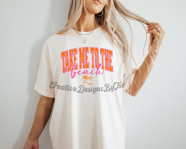 K&ouml;nnte beinhalten: Wei&szlig;es T-Shirt mit dem Text "Take Me To The Beach" in orangefarbener und rosafarbener Schrift. Unter dem Text befindet sich eine kleine Palme und ein Sonnenmotiv.