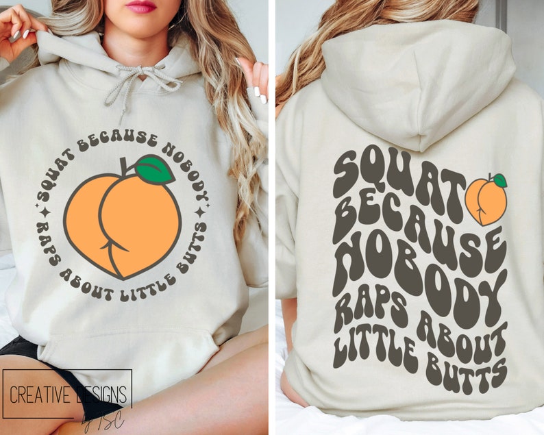 K&ouml;nnte beinhalten: Ein hellbeiger Hoodie mit einer Pfirsichgrafik und dem Text "Squat because nobody raps about little butts" in einer Retro-Schrift.
