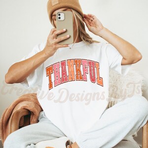 May include: White t-shirt with the word "THANKFUL" printed in a colorful retro font.