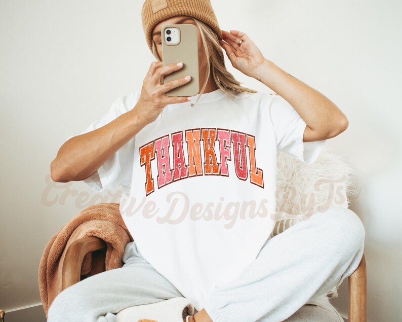 May include: White t-shirt with the word "THANKFUL" printed in a colorful retro font.