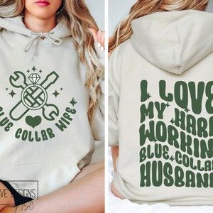 May include: A light beige hoodie with a green design on the front that says "Blue Collar Wife" with a wrench, screwdriver, and diamond ring. The back of the hoodie has a green design that says "I Love My Hard Workin' Blue Collar Husband".