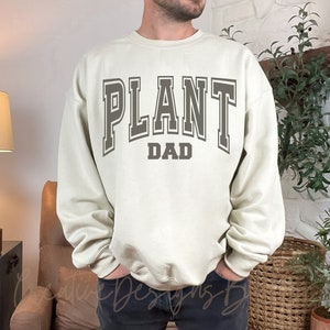 May include: A light beige sweatshirt with the text "PLANT DAD" in a gray varsity-style font.