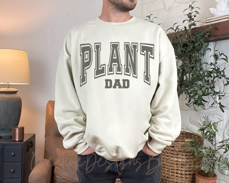 May include: A light beige sweatshirt with the text "PLANT DAD" in a gray varsity-style font.