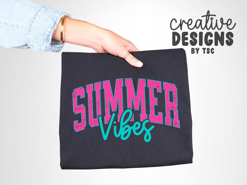 May include: A black t-shirt with the words "SUMMER Vibes" in a distressed pink font with a teal outline. The words are in a collegiate style font. The words "creative DESIGNS BY TSC" are in black script in the upper right corner.