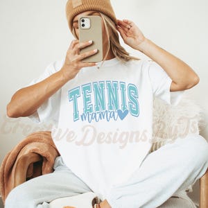 May include: White t-shirt with the text "Tennis Mama" in blue and teal lettering with a small blue heart.