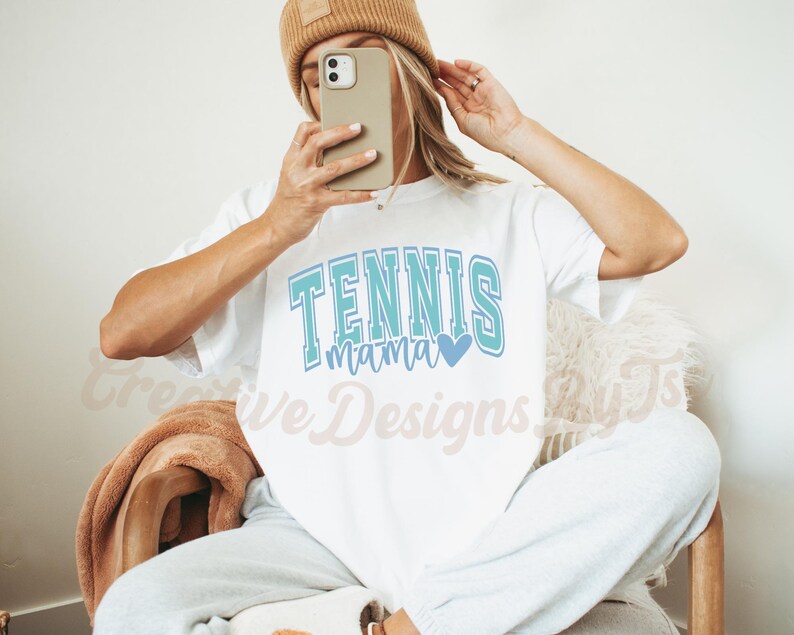 May include: White t-shirt with the text "Tennis Mama" in blue and teal lettering with a small blue heart.