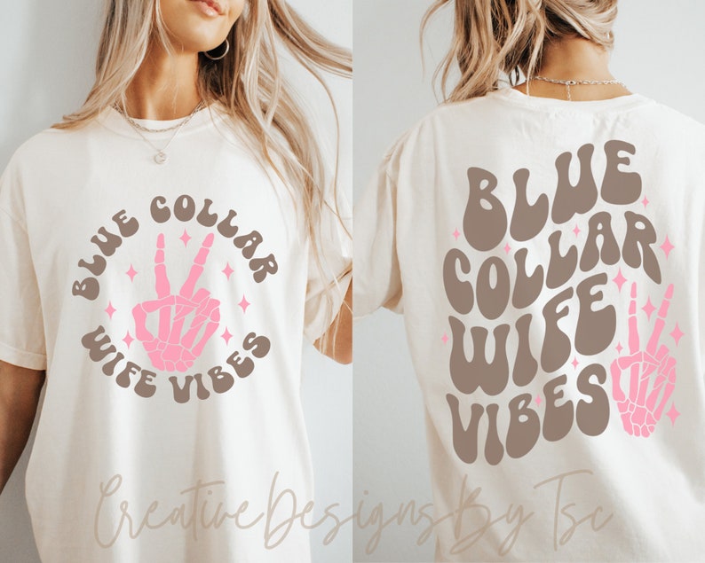 May include: A white t-shirt with the text "BLUE COLLAR WIFE VIBES" in brown and pink lettering with a pink skeleton hand making a peace sign in the center of the circle. The text is in a retro font style.