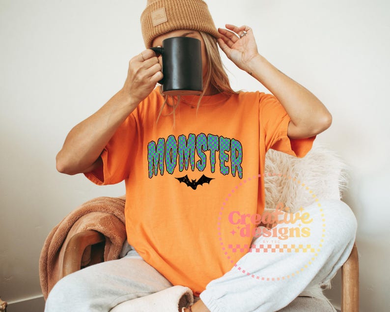 May include: Orange t-shirt with the word "MONSTER" in blue and green bubble letters and a black bat graphic. The shirt is part of a Halloween-themed collection.