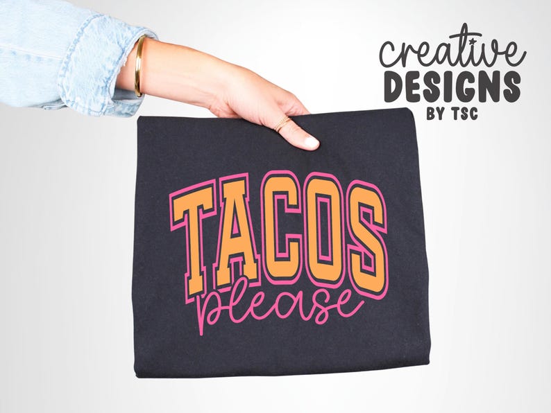 May include: A black t-shirt with the words "TACOS PLEASE" in orange and pink lettering. The text is in a collegiate style font. The words "creative designs by TSC" are written in a script font in the upper right corner.