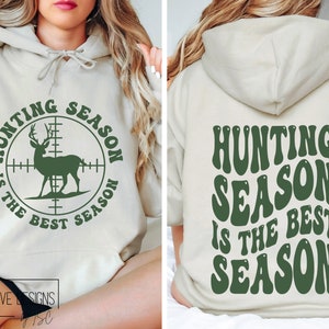 May include: A beige hoodie with the text "HUNTING SEASON IS THE BEST SEASON" in green. The front features a deer inside a crosshair circle. The back of the hoodie also displays the same text in a retro font.