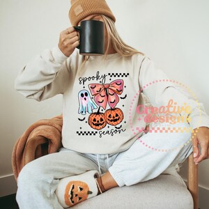 Puede incluir: Sudadera beige con un dise&ntilde;o de Halloween. El dise&ntilde;o incluye un fantasma, un lazo, dos calabazas y las palabras "spooky season". La sudadera se combina con pantalones de ch&aacute;ndal grises y un gorro color canela.