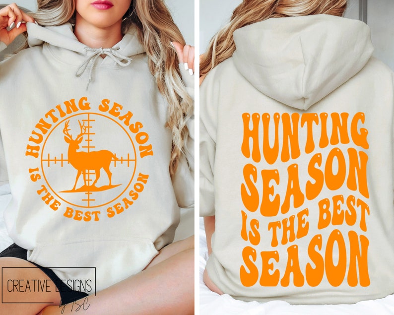 May include: A beige hoodie with orange text and graphics. The front features a deer silhouette inside a crosshair circle with the text "HUNTING SEASON IS THE BEST SEASON". The back of the hoodie repeats the phrase in a retro font.