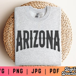Op de afbeelding: Een grijs sweatshirt met het woord "ARIZONA" in zwart op de voorkant. Het sweatshirt ligt op een geweven rieten oppervlak.