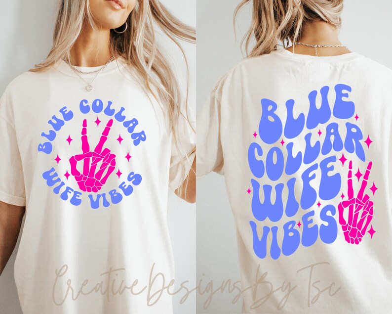 May include: A white t-shirt with the text "BLUE COLLAR WIFE VIBES" in blue and pink lettering with a pink skeleton hand making a peace sign in the center of the text. The text is in a retro font style.