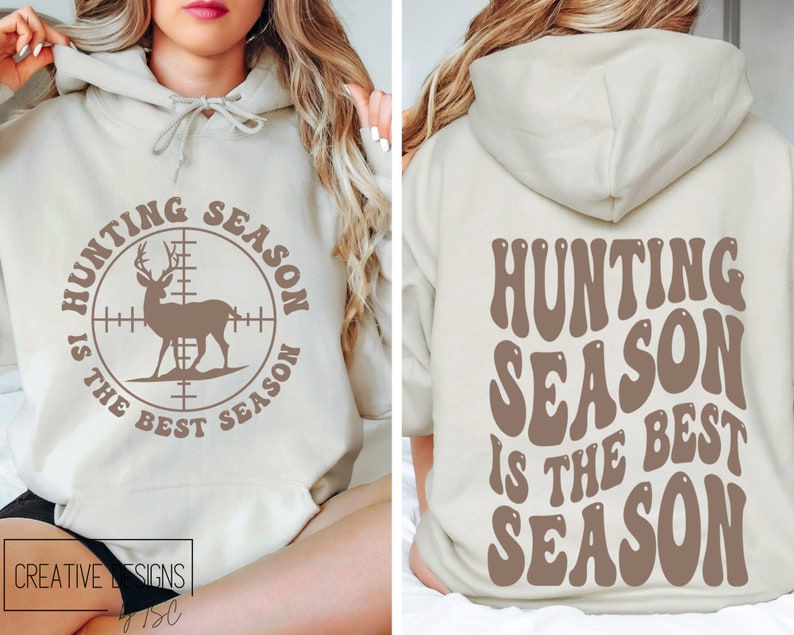 May include: Beige hoodie with the text "HUNTING SEASON IS THE BEST SEASON" on the front and back. The front design features a deer inside a crosshair circle. The back design has the same text in a retro font.