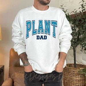 May include: White sweatshirt with blue text that reads "PLANT DAD" in a varsity style font.