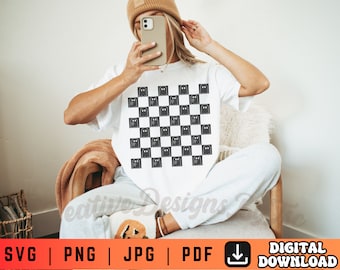 May include: A white t-shirt with a black and white checkered pattern featuring a ghost design. The shirt is being worn by a person with a brown beanie.