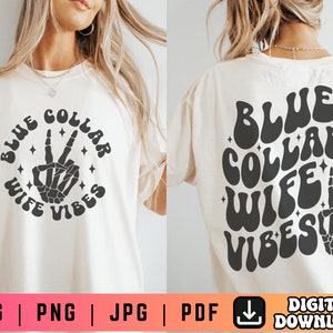 May include: A white t-shirt with a black graphic design that says "Blue Collar Wife Vibes" in a retro font. The graphic also includes a peace sign made of a skeleton hand.