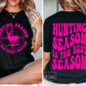 May include: Black t-shirt with the text "HUNTING SEASON IS THE BEST SEASON" in bright pink. The front of the shirt features a pink deer graphic inside a target reticle. The back of the shirt has the same text in a wavy font.