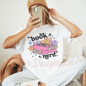 May include: White t-shirt with the text "book nerd" in black and a stack of books with pink and white checkered covers and colorful flowers.