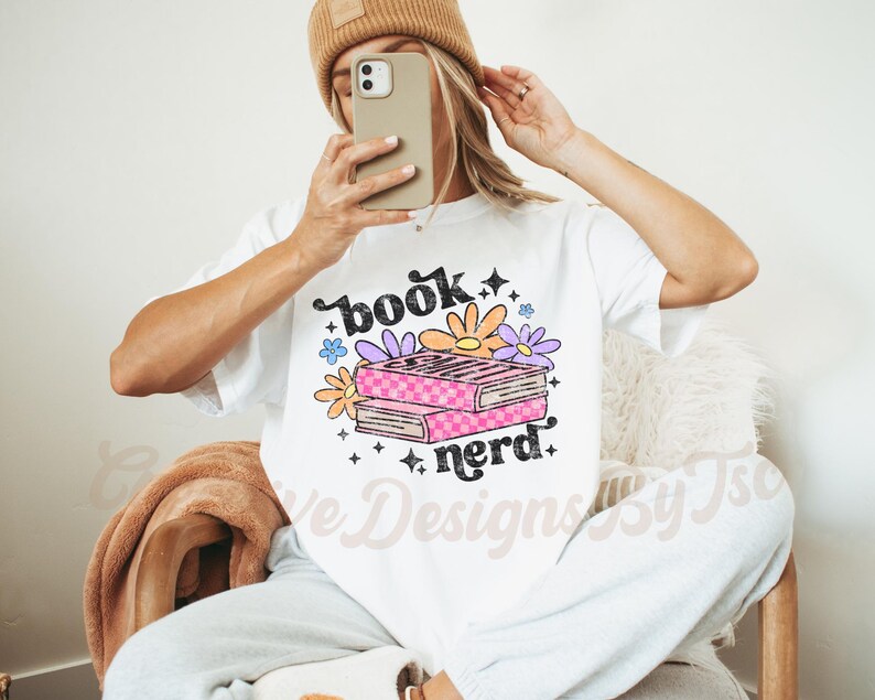 May include: White t-shirt with the text "book nerd" in black and a stack of books with pink and white checkered covers and colorful flowers.