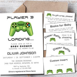 May include: A white baby shower invitation card featuring a green video game controller graphic and the text PLAYER 3 LOADING. The set includes matching insert cards for a diaper raffle, books for baby, and gift wrap requests, all with a pixelated font.