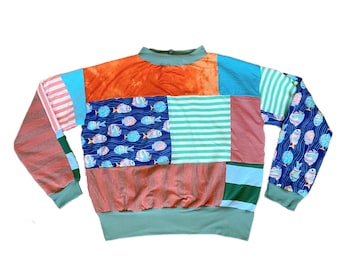 May include: A long-sleeved, patchwork sweater with a variety of colors and patterns, including orange, blue, green, and pink. The sweater has a crew neck and a ribbed hem. The fabric is a mix of cotton and polyester.