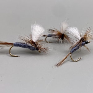 May include: Three fly fishing lures with brown and white feathers and a blue body.