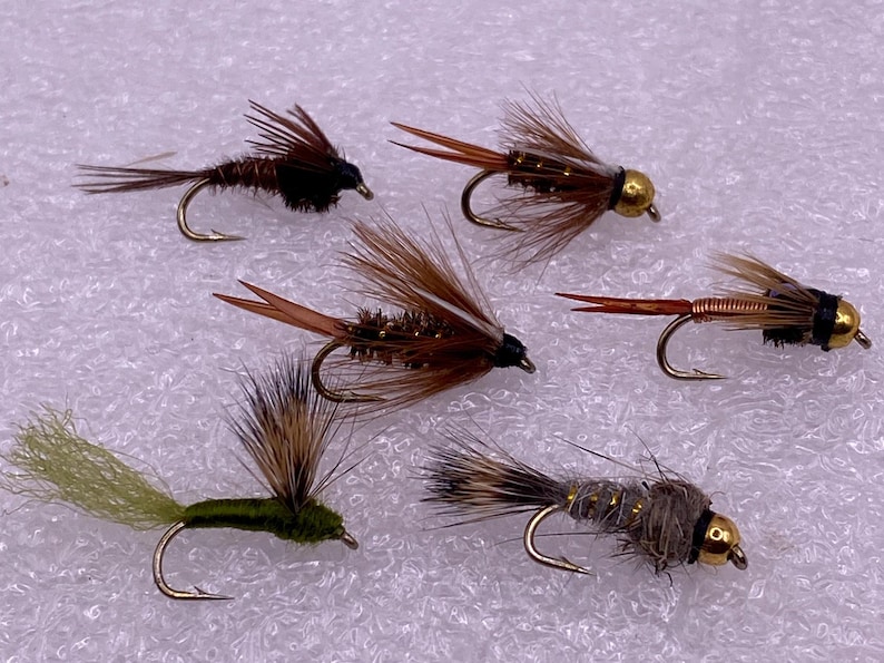 May include: Five different fly fishing lures with brown, gold, and green feathers and a black head. The lures have gold beads on the end of the hook.