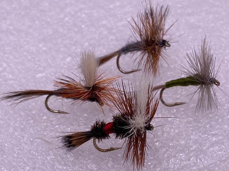 May include: Four fly fishing lures with brown, white, and green feathers. The lures have gold hooks.