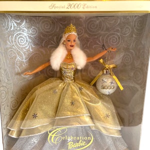 Może przedstawiać: Złota i srebrna lalka Barbie w białej futrzanej szalce, trzymająca srebrną ozdobę z napisem 2000. Lalka znajduje się w pudełku z napisem "Celebration Barbie" i "Special 2000 Edition".
