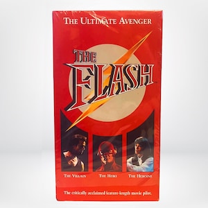 Może przedstawiać: Czerwona kaseta VHS z żółtym błyskawicą i tekstem "THE FLASH" w kolorze białym. Tekst "THE ULTIMATE AVENGER" znajduje się na górze kasety. Kaseta zawiera trzy zdjęcia postaci: złoczyńcy, bohatera i bohaterki. Tekst "The critically acclaimed feature-length movie pilot." znajduje się na dole kasety.