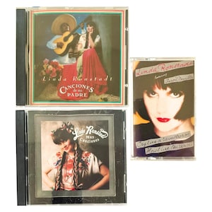 Op de afbeelding: Drie muziekalbums met Linda Ronstadt. Twee cd's tonen albumhoezen met Ronstadt in traditionele kleding, met de tekst "Canciones de mi Padre" en "Mas Canciones". Een cassettebandje met Ronstadt en Aaron Neville.