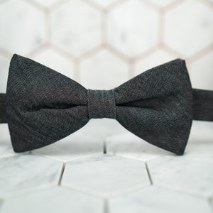 May include: A black bow tie made of a textured fabric. The bow tie is on a white background.
