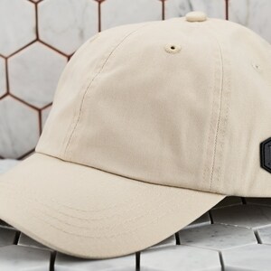 May include: A beige baseball cap with a black leather patch featuring the letters "DM" in a hexagonal shape.