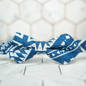 May include: A blue and white bow tie with a geometric pattern. The bow tie is made of fabric and has a white background with blue geometric shapes.