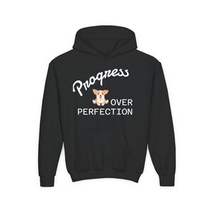 May include: Black hooded sweatshirt with the words "Progress Over Perfection" in white script. A cartoon corgi dog is in the center of the design. The sweatshirt has a front pocket and a drawstring hood.