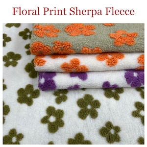 May include: A stack of four fabric swatches with different floral prints. The top swatch is a light green fabric with orange flowers. The second swatch is white with orange flowers. The third swatch is white with purple flowers. The bottom swatch is white with green flowers.