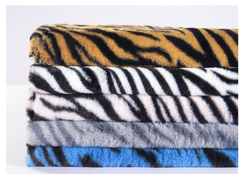 May include: A stack of five fabric swatches with different animal print patterns. The top swatch is a brown and black tiger print, followed by a black and white zebra print, a pink and black zebra print, a gray zebra print, and a blue and black zebra print.