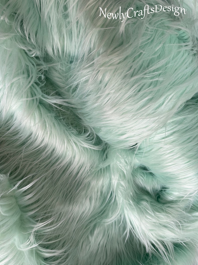 May include: Close-up of a soft, light green faux fur fabric. The fur is long and fluffy, creating a luxurious and plush texture.