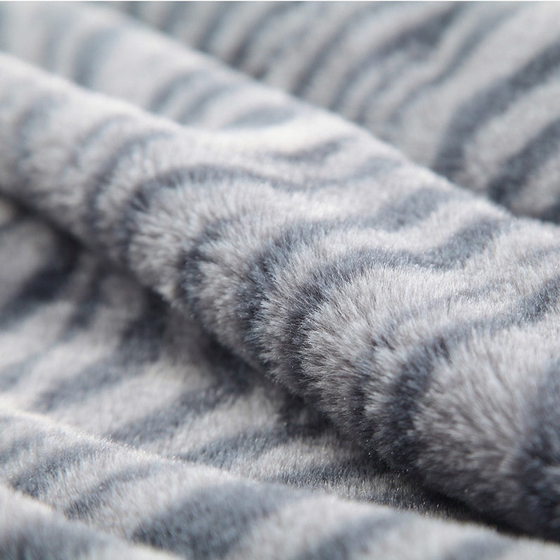 May include: Close-up of a soft, gray and white faux fur fabric with a zebra stripe pattern.