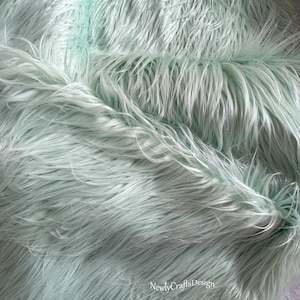 May include: A close-up of a light green faux fur fabric. The fabric is soft and fluffy, with a long pile.